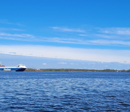 Kuvassa merimaisemaa, taustalla näkyy mannerta, ja vasemmalla kaukana satamassa oleva rahtilaiva.
