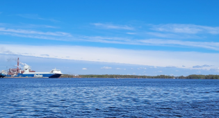 Kuvassa merimaisemaa, taustalla näkyy mannerta, ja vasemmalla kaukana satamassa oleva rahtilaiva.