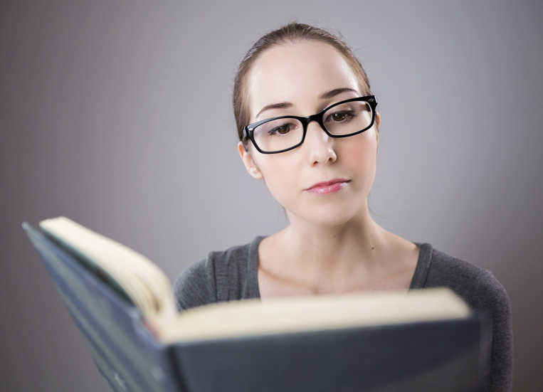 Kuvassa silmälasipäinen nuori henkilö lukee kirjaa.