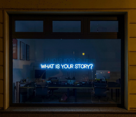 A picture of a window, where you can barely see an office. There is a lightened sentence saying What is your story=