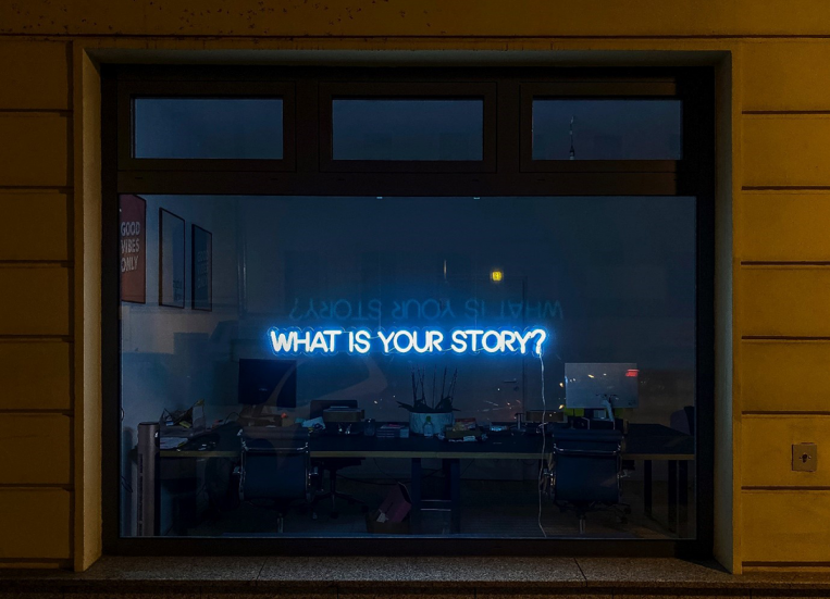 A picture of a window, where you can barely see an office. There is a lightened sentence saying What is your story=