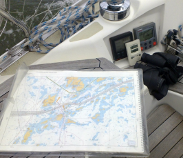 Näkymä purjeveneen kannelta, pääosassa muovikotelossa oleva merikorttisarja.