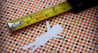 Kuvassa paperista leikattu hahmo, jonka vieressä mitta.