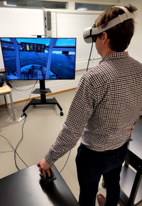 Kuvassa henkilöllä on päässään VR-lasit ja hän ohjaa kahdella ohjausvivulla satamahinaajaa.